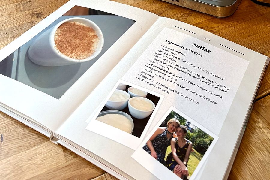El libro de recetas abierto de Sarah está sobre la encimera de la cocina, mostrando su formato de libro layflat, con imágenes de arroz con leche turco en la página izquierda y la receta familiar correspondiente en la derecha, ilustrando el consejo de Hofmann de elegir un diseño layflat fácil de usar mientras se cocina.