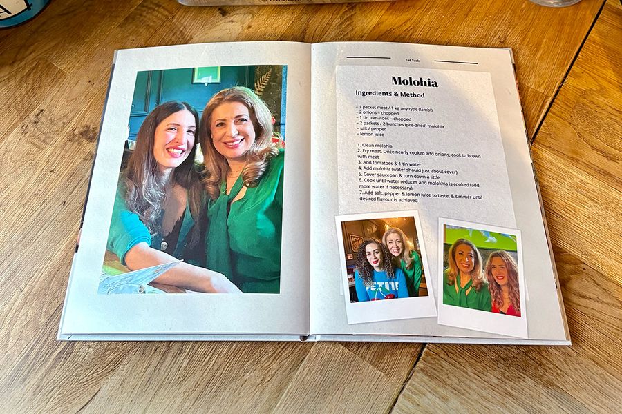 Una doble página del libro de recetas personalizado de Sarah muestra una receta de molohia, acompañada de fotos familiares en lugar de una imagen del plato, ilustrando el consejo de Hofmann de incluir fotos personales que hagan un libro de recetas verdaderamente significativo.