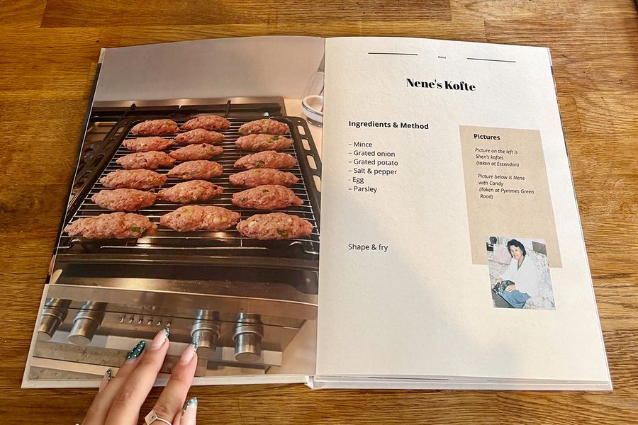 Una doble página abierta del libro de recetas de Sarah muestra la receta de kofte de su Nene, con la mano manicurada de una mujer descansando sobre el libro en una encimera de madera, ilustrando los últimos consejos de Hofmann antes de imprimir un libro de recetas personalizado.