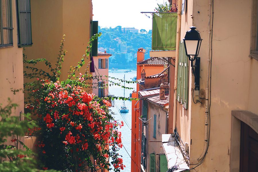 Una calle estrecha llena de flores conduce hacia el mar en Niza, capturando el encanto de unas vacaciones de septiembre en el sur de Francia.