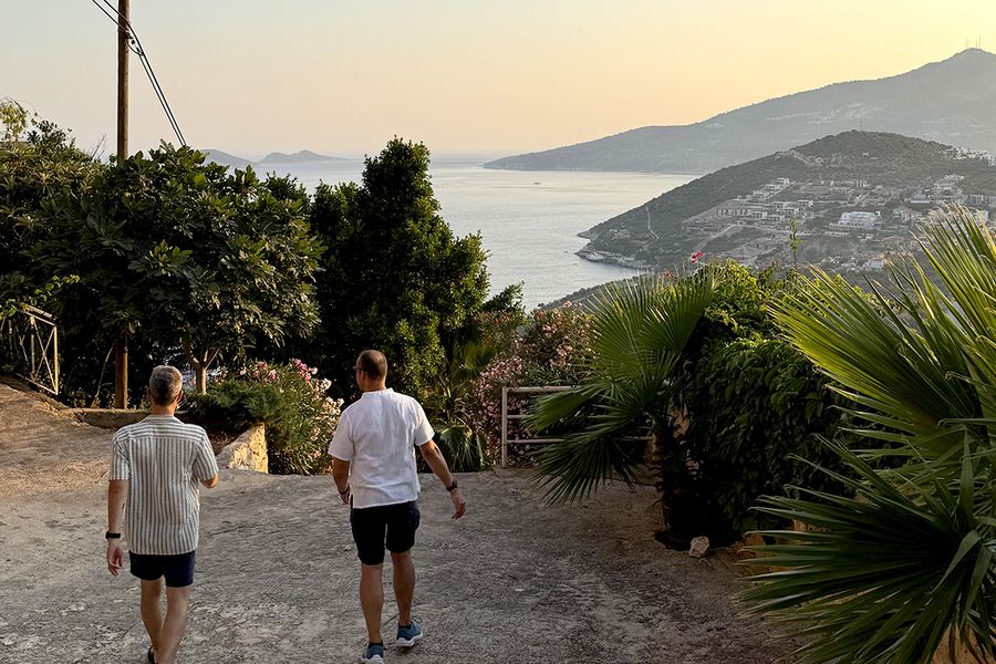 Dos hombres bajan por una colina rodeada de plantas hacia el mar en Kalkan, capturando el encanto de unas vacaciones de septiembre en Turquía en la Costa Turquesa.