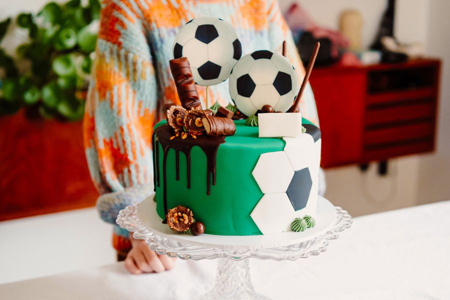 Una tarta de cumpleaños infantil decorada con balones de fútbol y barritas de chocolate, ilustrando el consejo de Hofmann de fotografiar la tarta protagonista antes de que lleguen los invitados.