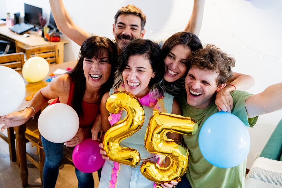 Un grupo de jóvenes se agrupa alrededor de globos con el número '25', sonriendo y posando para una foto, ilustrando los consejos de Hofmann para captar los momentos de un cumpleaños importante.