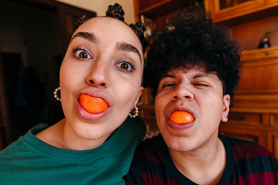 Una pareja hace muecas divertidas con rodajas de naranja en la boca, ilustrando las ideas de Hofmann para mensajes graciosos que escribir en una tarjeta de aniversario de bodas.