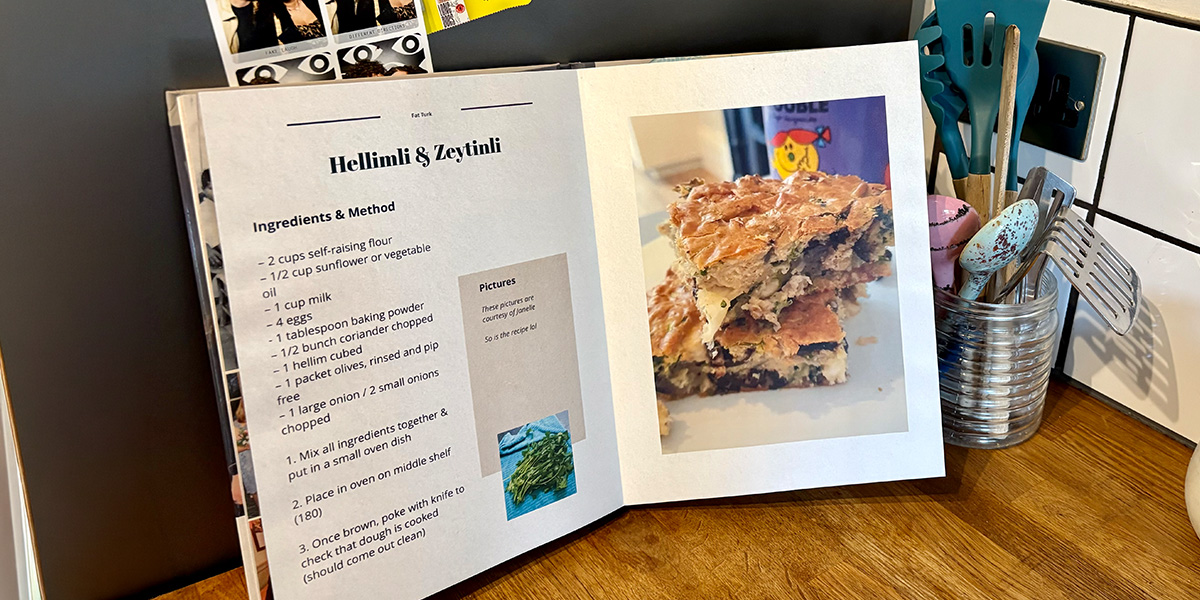 Un libro de recetas personalizado abierto se encuentra en una cocina, con un tarro de cucharas y utensilios de cocina de fondo, presentando la guía de Hofmann para crear tu propio recetario personalizado.
