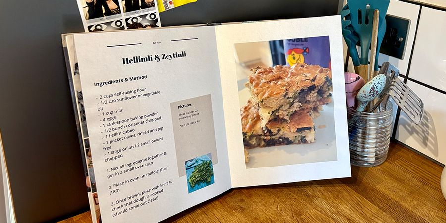 Un libro de recetas personalizado abierto se encuentra en una cocina, con un tarro de cucharas y utensilios de cocina de fondo, presentando la guía de Hofmann para crear tu propio recetario personalizado.