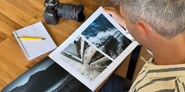 El fotógrafo Charl van Rooy mira su portafolio, con su cámara y una libreta sobre la mesa a su lado, presentando la guía de Hofmann para crear un portafolio de fotografía en formato álbum de fotos.