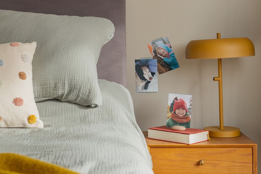 Una selección de impresiones de fotos familiares cuelga de la pared junto a una cama, ilustrando cómo las fotos impresas de Hofmann aportan un toque acogedor y personal a un dormitorio hygge.