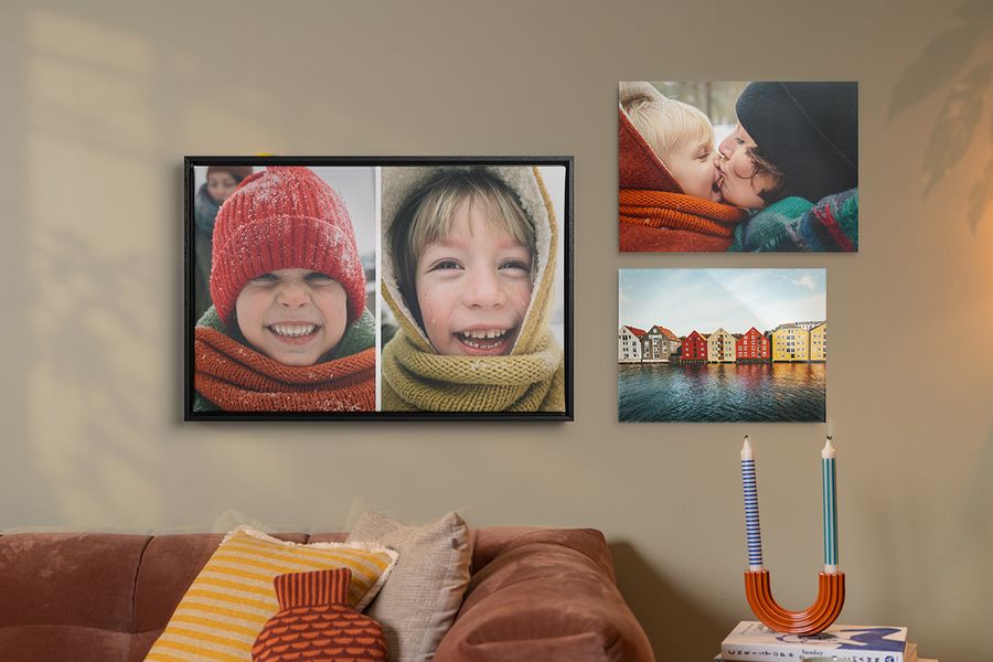 Tres ejemplos de decoración de pared personalizada cuelgan sobre un sofá en un salón, láminas familiares otoñales con niños sonrientes con ropa de invierno, ilustrando cómo la decoración de pared de Hofmann aporta un estilo hygge acogedor al hogar.
