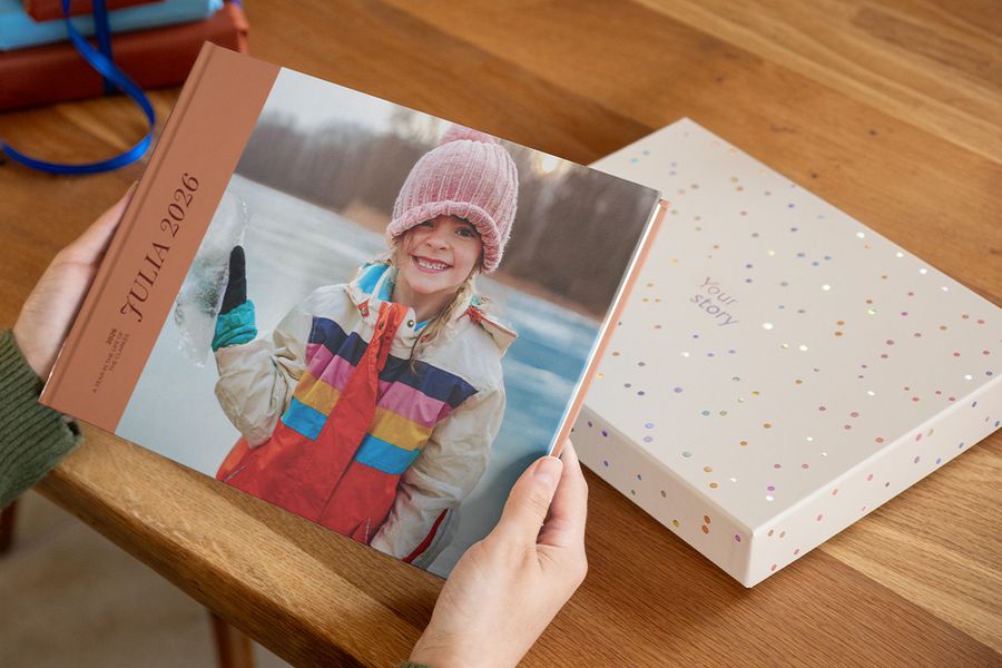 Alguien sostiene un álbum de fotos titulado 'Julia', con una niña sonriente en la portada, con una caja de regalo de presentación justo detrás sobre la mesa, ilustrando por qué una caja para álbum de fotos hace que una creación se sienta aún más especial.