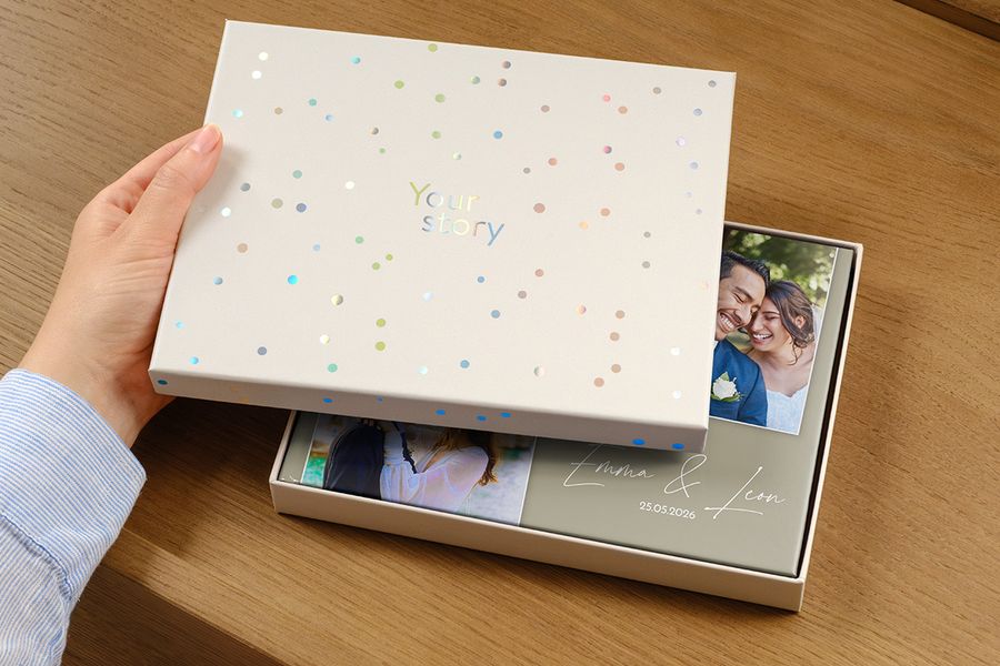 Un álbum de fotos de boda está dentro de la nueva caja de presentación, con una foto de la pareja en la portada y la fecha de la boda como título, parcialmente oculta por la tapa entreabierta de la caja de regalo, ilustrando por qué una caja de presentación merece la pena para un álbum de boda premium.