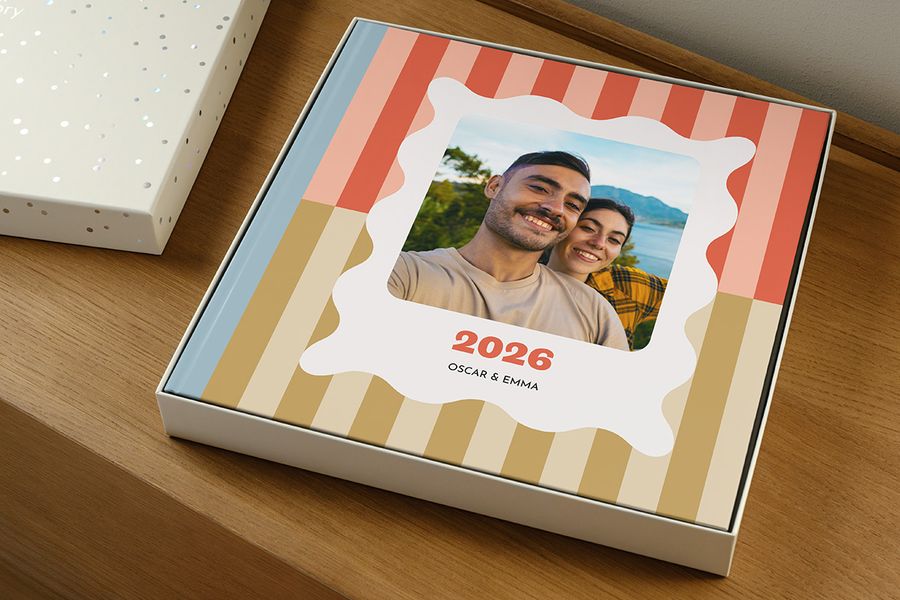 Un álbum de fotos reposa dentro de la caja de regalo sin la tapa, pareciendo un anuario etiquetado como '2026' con una pareja sonriente en la portada, ilustrando cómo elegir el tamaño adecuado de caja de presentación para tu álbum de fotos.
