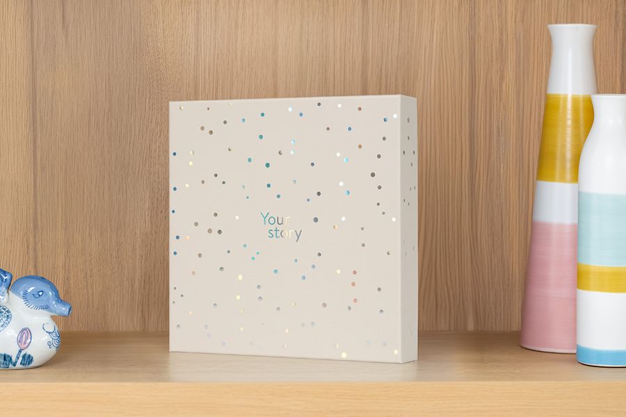 La caja de presentación está sobre una estantería junto a un jarrón y otros objetos decorativos, ilustrando cómo también funciona como una atractiva caja de almacenamiento para álbumes de fotos.