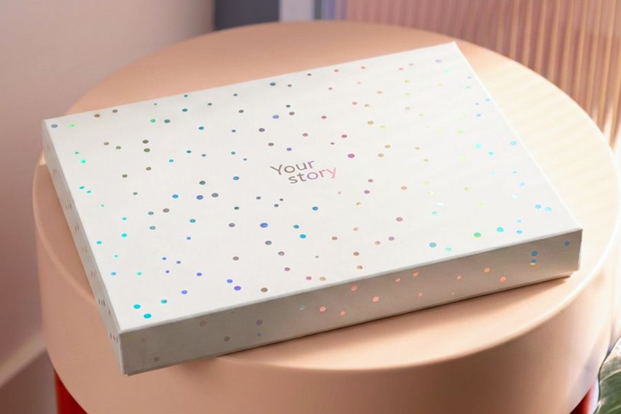 La caja de presentación cerrada descansa sobre un taburete, mostrando el acabado final de la nueva caja regalo para álbumes de fotos de Hofmann.