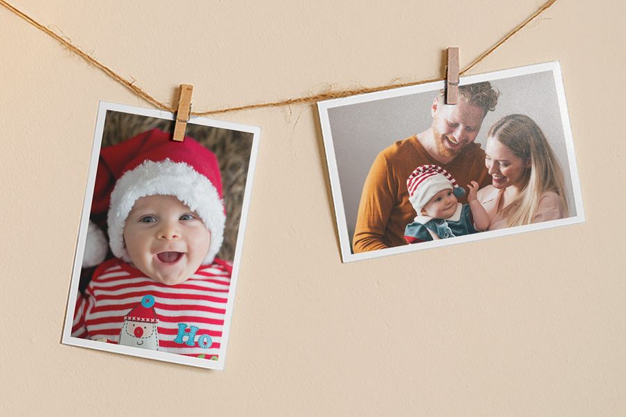 Impresiones de fotos colgadas de una cuerda con pinzas, una con un bebé sonriente con un gorro navideño y otra con un hombre y una mujer sonrientes sosteniendo a un bebé vestido con un conjunto navideño, para ilustrar los consejos de Hofmann para convertir una foto favorita en un adorno de Navidad casero.