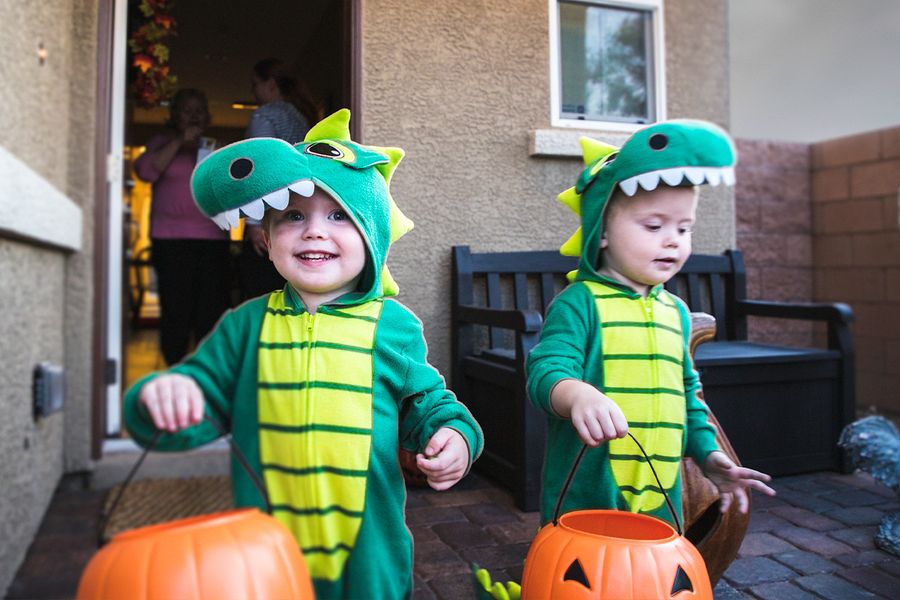 Dos niños pequeños disfrazados de dinosaurio piden caramelos con cestas en forma de calabaza, ilustrando las frases de Halloween de Hofmann para fotos de truco o trato.
