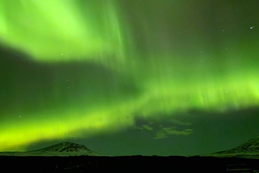 Montañas nevadas bajo un cielo teñido de verde intenso por la aurora boreal, que ilustra los consejos de Hofmann sobre dónde ver la aurora boreal sin ir a Islandia.