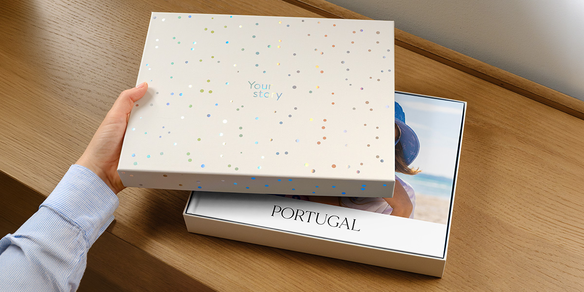 Una caja de presentación de Hofmann está con la tapa entreabierta, dejando ver un álbum de fotos de viaje personalizado de Portugal en su interior, con la portada parcialmente oculta por la tapa, presentando la nueva caja regalo para álbumes de fotos de Hofmann.