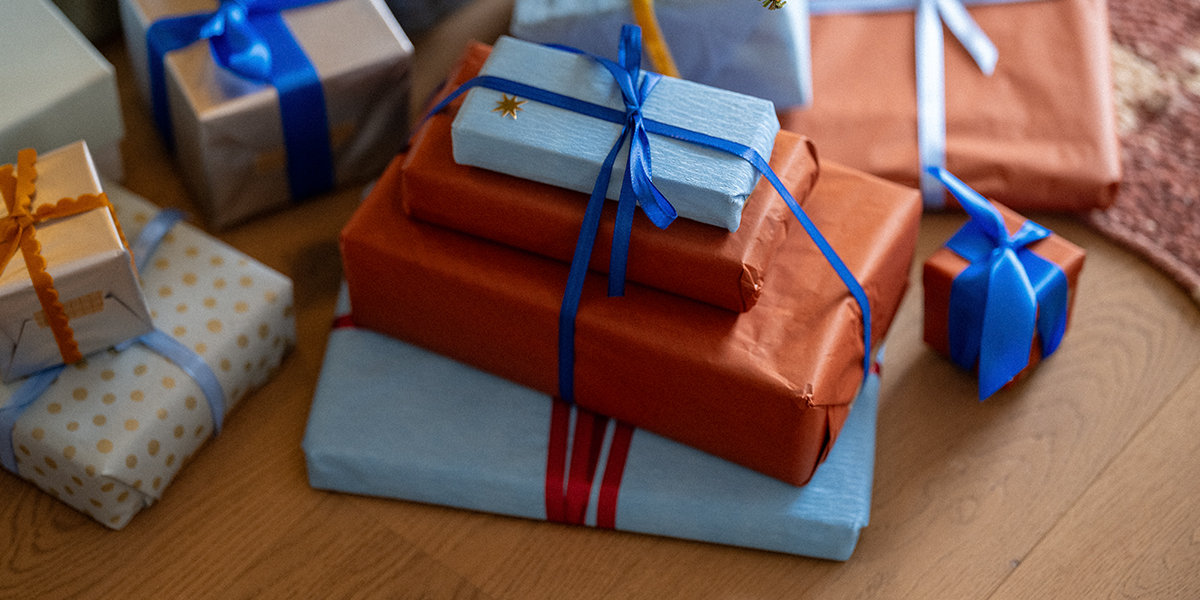 Una pila de regalos envueltos en papel naranja y azul claro, con cintas azules sobre un suelo de madera, ilustrando los consejos de Hofmann para regalos de Navidad en el Black Friday.