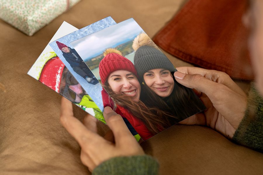 Persona sosteniendo impresiones de fotos en las manos, con una en primer plano en la que aparecen dos mujeres sonrientes con gorros y abrigos de invierno, para ilustrar los consejos de Hofmann para encontrar las fotos adecuadas para un regalo personalizado con fotos.