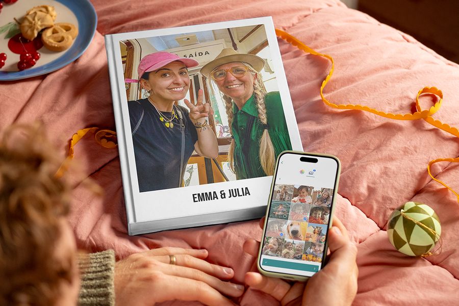 Álbum de fotos personalizado titulado “Emma and Julia” con una madre y su hija adulta en la portada, junto a las manos de un hombre que sostiene un teléfono para mostrar lo fácil que es seleccionar fotos y crear un álbum de fotos de Hofmann, para ilustrar los consejos de Hofmann para reunir las fotos de familiares y amigos para un regalo personalizado.