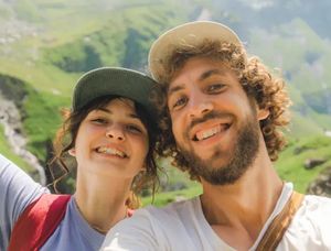 Una pareja sonriente en un paisaje montañoso durante una aventura de verano, perfecta para elegir frases para fotos de verano en Instagram o en un álbum de fotos de Hofmann.