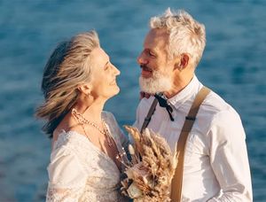 Una pareja mayor y feliz en la playa, vestida de forma elegante, que inspira ideas sobre qué escribir en una tarjeta de Bodas de Oro.