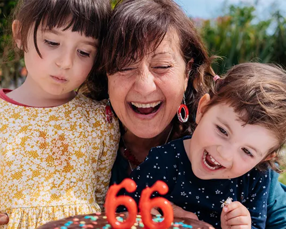 Una abuela celebra su 66 cumpleaños con sus dos nietos a su lado, a punto de soplar las velas de su tarta, como inspiración para ideas de regalos de cumpleaños de la guía definitiva de regalos de cumpleaños de Hofmann.
