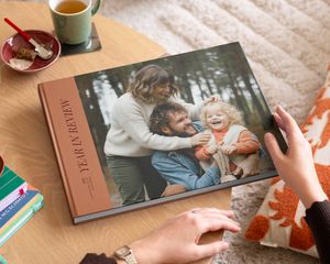 Un álbum decorativo de Hofmann de tipo coffee table book con un repaso del año y una bonita foto familiar en la portada, colocado sobre una mesa de centro como inspiración para un álbum decorativo personalizado.
