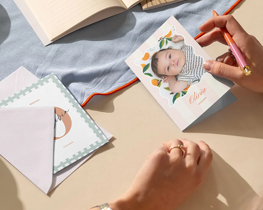 Unas manos escriben una tarjeta personalizada con fotos de bebé en un escritorio.