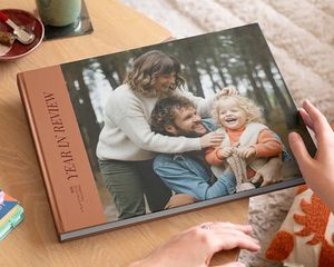 Un álbum decorativo de Hofmann de tipo coffee table book con un repaso del año y una bonita foto familiar en la portada, colocado sobre una mesa de centro como inspiración para un álbum decorativo personalizado.
