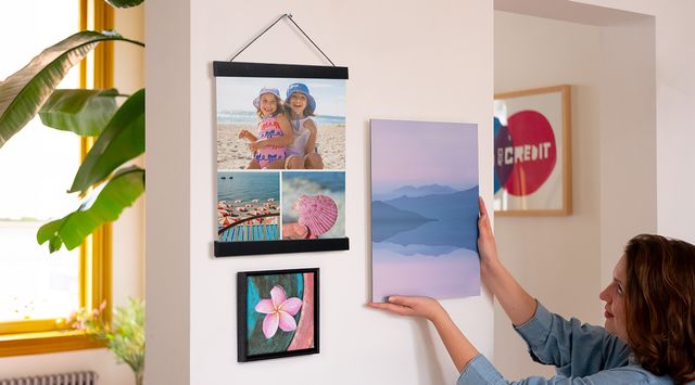 Una persona cuelga una foto junto a dos impresiones enmarcadas.